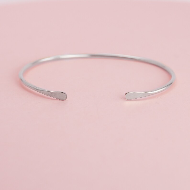 May include: A simple silver bangle bracelet with rounded ends. The bracelet is open and ready to be worn.