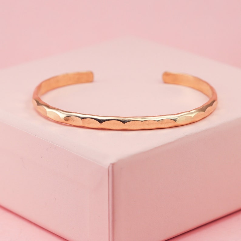 May include: A hammered gold-toned bangle bracelet. The bracelet is simple and delicate, with a smooth, rounded finish.