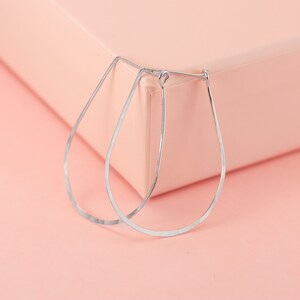 May include: A pair of silver teardrop-shaped hoop earrings. The earrings are made of a thin, hammered metal and have a simple, elegant design.