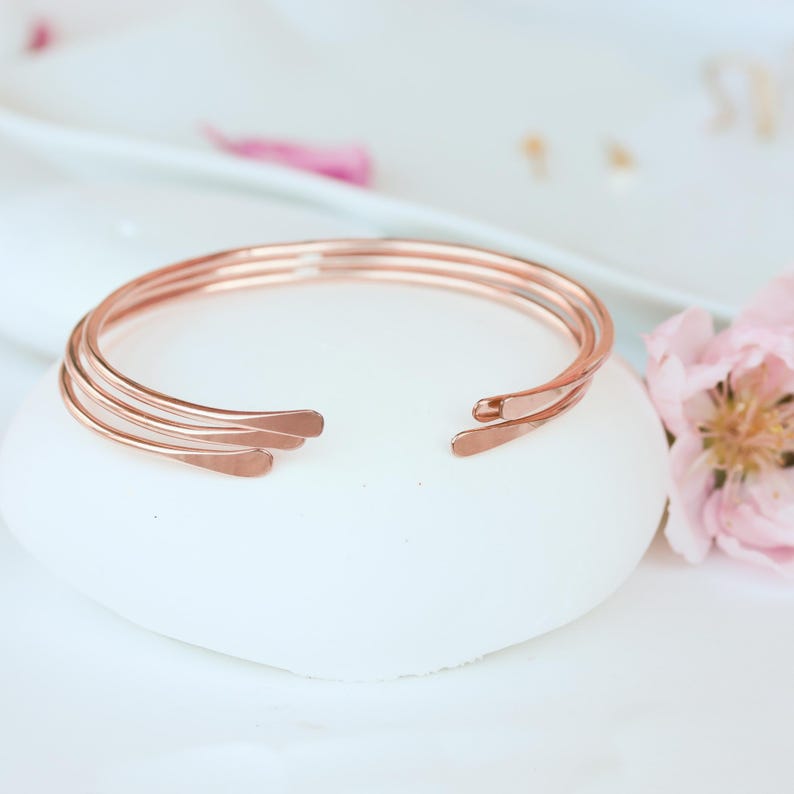 May include: A set of three rose gold bangle bracelets. The bracelets are stacked on top of each other and are made of a thin, delicate metal.
