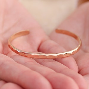 May include: A rose gold hammered bangle bracelet. The bracelet is simple and elegant, with a smooth, polished finish.