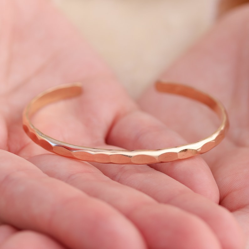 May include: A rose gold hammered bangle bracelet. The bracelet is simple and elegant, with a smooth, polished finish.