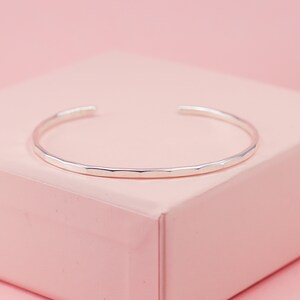 May include: A silver hammered bangle bracelet. The bracelet is simple and delicate, with a smooth, polished finish.