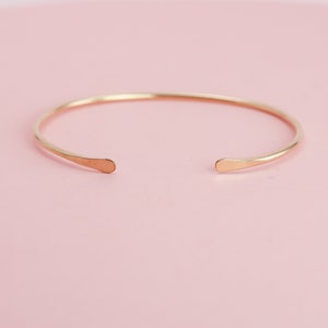 May include: A simple gold bangle bracelet with rounded ends. The bracelet is made of a thin, smooth metal and has a minimalist design.
