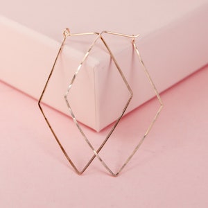 May include: A pair of gold-toned diamond-shaped hoop earrings. The earrings are made of thin metal and have a simple, elegant design.