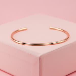 May include: A simple, rose gold bangle bracelet. The bracelet is made of a smooth, polished metal and has a minimalist design.