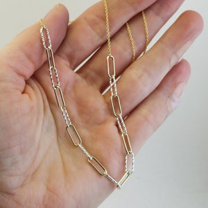 May include: A gold chain necklace with a textured silver chain. The necklace has a delicate, dainty look.