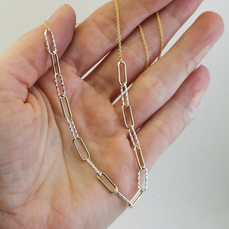 May include: A gold chain necklace with a textured silver chain. The necklace has a delicate, dainty look.