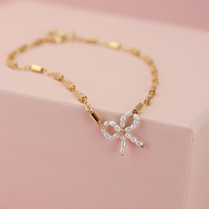 May include: A gold chain bracelet with a pearl bow charm. The bracelet is delicate and feminine.