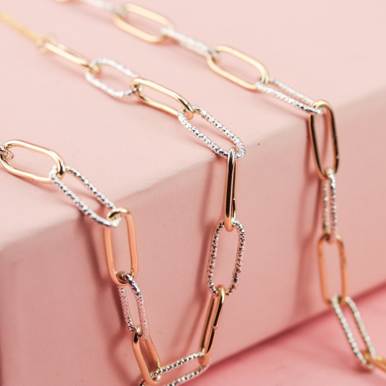 May include: A gold and silver chain necklace with oval links. The chain is made of two different metals, with one side being gold and the other side being silver.