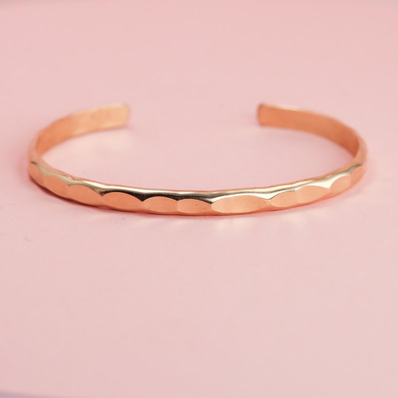 May include: A gold hammered bangle bracelet. The bracelet is simple and delicate, with a smooth, polished finish.