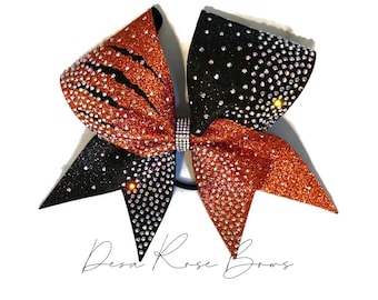 May include: A black and orange cheer bow with a tiger stripe design and rhinestones. The bow is tied with a black elastic band.