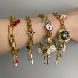 May include: Four gold charm bracelets with various charms, including a star, a lock, a cherry, an anchor, a fish, a letter I, a letter A, and a square charm with a star design.
