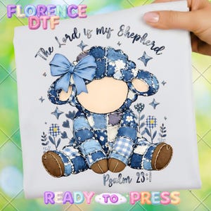 May include: A white fabric with a patchwork sheep design. The sheep is blue with a light blue bow, and the text "The Lord is my Shepherd" and "Psalm 23:1" are printed on the fabric. The words "READY TO PRESS" are also printed on the fabric.