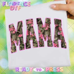 May include: White t-shirt with the word "MAMA" in large, bold letters. The letters are filled with a camouflage pattern and pink leaves, outlined in pink. The text "READY TO PRESS" is at the bottom.
