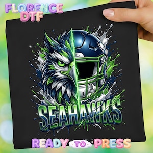 May include: Black graphic featuring a stylized Seattle Seahawks football helmet and eagle design. The image includes the team name in green and white, with the words "READY TO PRESS" at the bottom. The design is on a black background.