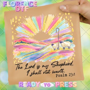 Peut inclure: Un transfert prêt à presser de couleur beige avec un motif coloré. Le motif représente un paysage avec deux moutons, une crosse de berger et un éclat de soleil rayonnant. Le texte dit "Le Seigneur est mon berger, je ne manquerai de rien. Psaume 23:1."