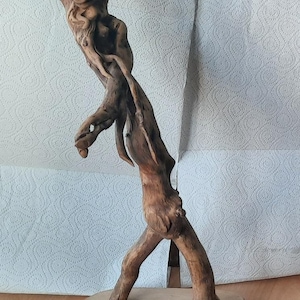 May include: A wooden sculpture of a whimsical creature with a pig-like face and long, spindly legs. The sculpture is standing on a wooden base.