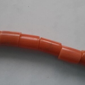 May include: Close-up of a strand of orange beads. The beads are cylindrical and evenly spaced, creating a smooth, curved line. The beads have a glossy finish and a consistent color throughout.