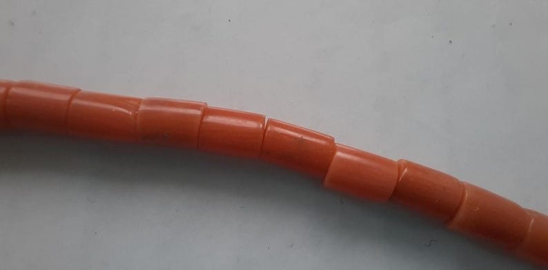 May include: Close-up of a strand of orange beads. The beads are cylindrical and evenly spaced, creating a smooth, curved line. The beads have a glossy finish and a consistent color throughout.