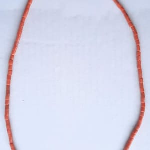 May include: A necklace composed of small, rectangular coral-colored beads. The beads are strung together to form a continuous loop. The necklace is displayed against a white background, highlighting its color and design.