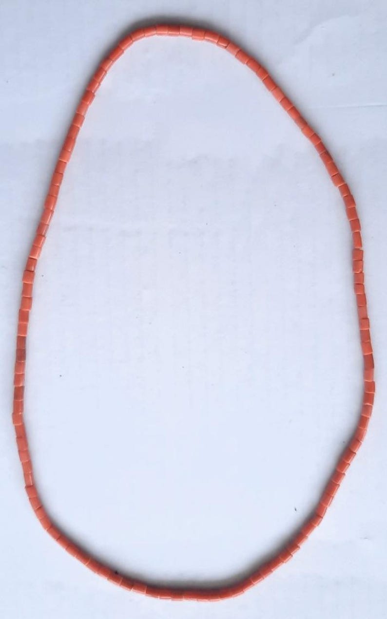 May include: A necklace composed of small, rectangular coral-colored beads. The beads are strung together to form a continuous loop. The necklace is displayed against a white background, highlighting its color and design.