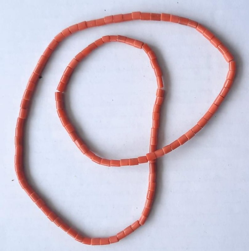 May include: A necklace composed of small, rectangular coral beads in a vibrant orange hue. The beads are strung together, forming a continuous loop. The necklace is displayed against a plain white background.