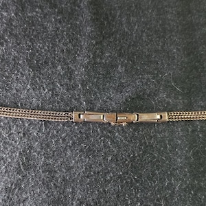 May include: A gold-toned watch band with a chain-link design. The band has a rectangular clasp in the center and two smaller clasps on each end. The band is approximately 7 inches long.