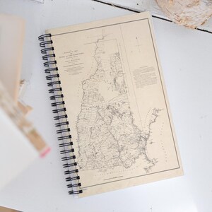 May include: A vintage spiral bound notebook with a map of the state of New Hampshire printed on the cover. The map is in black and white and shows the state's major cities and towns.