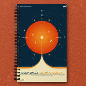 May include: A blue and orange notebook with a spiral binding. The cover features a graphic of a clock with a red circle and a white line in the center. The text "DEEP SPACE ATOMIC CLOCK" is printed in white on the bottom of the cover. The text "BETTER CLOCKS BETTER NAVIGATION BETTER SCIENCE" is printed in white below the main title. The text "EXPLORE" is printed in white at the bottom left corner of the cover.