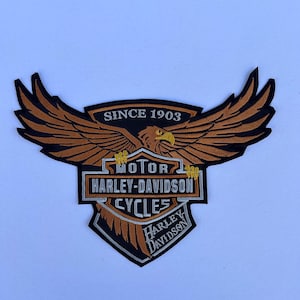 Könnte beinhalten: Ein braunes und schwarzes gesticktes Patch mit einem Harley-Davidson-Adlerlogo. Das Patch trägt die Worte "Motor Harley-Davidson Cycles" und "Since 1903".