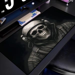 May include: A black and white graphic design of a skull wearing a helmet and headphones. The skull is wearing a flight suit with a zipper and a breathing apparatus. The design is on a black background.