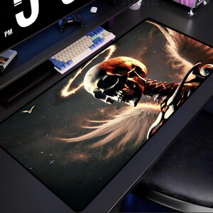 May include: A black gaming mouse pad with a dark galaxy background and a skull with angel wings in the center. The skull is glowing orange and yellow.