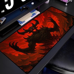 May include: A large rectangular mouse pad featuring a detailed illustration of a demonic figure with glowing red eyes against a fiery red background. The black demon has large horns and outstretched claws. A keyboard and monitor are visible in the background.