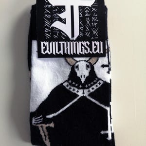 May include: Black and white socks featuring a graphic of a horned figure in a black robe. The socks have the text "EVILTHINGS.EU" on the tag. The socks are folded and packaged.