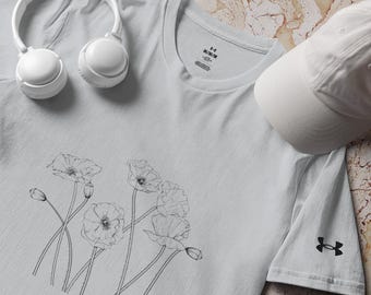 Può includere: Una t-shirt grigio chiaro a maniche corte con un'illustrazione a linee nere di fiori di papavero sul davanti. La maglia presenta un girocollo, un'etichetta di taglia M e un logo Under Armour nero sulla manica, accompagnata da cuffie e cappellino bianchi.