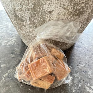 K&ouml;nnte beinhalten: Eine durchsichtige Plastikt&uuml;te gef&uuml;llt mit kleinen, quadratischen, braunen Karamellbonbons.