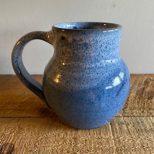 May include: A blue ceramic mug with a speckled glaze. The mug has a rounded body and a handle.