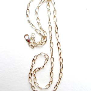 May include: A silver-toned metal chain necklace featuring elongated oval links. The necklace includes a lobster claw clasp mechanism at one end, allowing for secure fastening. The chain has a polished finish that reflects light across its surface.