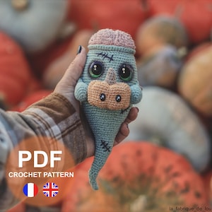 May include: Crochet pattern PDF for a blue and pink ghost amigurumi with stitched eyes and a stitched mouth. The pattern is available in both French and English.