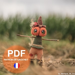 May include: Crochet pattern for a pumpkin scarecrow amigurumi doll. The doll is wearing a green shirt and brown pants. The pattern is in French and includes a PDF download.