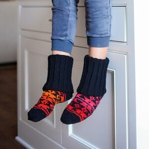 May include: A woman wearing a black cardigan, blue jeans, and colorful knitted socks sits on a white kitchen counter.