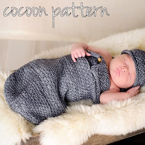 May include: A gray knitted baby cocoon swaddle with a white hat. The baby is sleeping peacefully on a white faux fur surface.