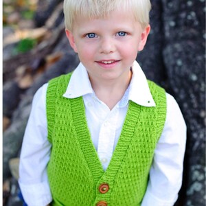 May include: A young child wearing a bright green knitted vest with wooden buttons over a white collared shirt and blue jeans. The word "pattern" is in the top left corner. The child is smiling at the camera.