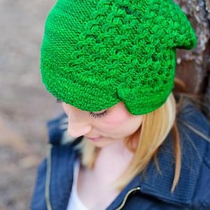 Puede incluir: Un gorro de punto verde brillante con un patrón texturizado. El gorro está hecho de un hilo suave y tiene un ajuste ceñido. El gorro es de un tono verde vibrante y es adecuado para climas fríos.