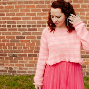 Può includere: Una donna indossa un maglione fuzzy a righe rosa e bianche con un orlo arricciato e una gonna di tulle rosa brillante.