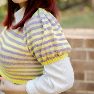 May include: A striped yellow and purple knit sweater with puffed sleeves. The sweater is cropped and has a relaxed fit.