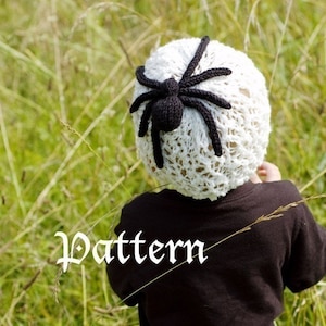 Puede incluir: Un gorro blanco de ganchillo con una araña negra en la parte superior. El gorro lo lleva puesto un niño de pie en un campo de hierba alta. La palabra "Pattern" está escrita en blanco sobre la hierba.