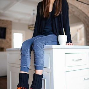May include: A pair of black knit socks with a patterned design in red, orange, and pink. The socks are thick and appear to be made of wool or a similar material. The socks are worn with blue pants.