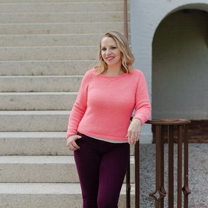 Può includere: Una donna con un maglione rosa e jeans viola scuro sta in piedi su una serie di gradini di cemento. Si appoggia a un corrimano di metallo.